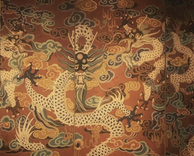 A painted Chinese dragon coiling through clouds on an ochre temple mural